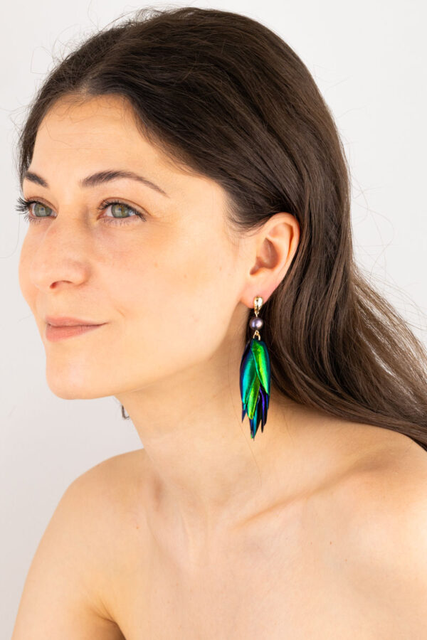 Close-up of peacock pearl beetle earrings showing colorful reflections on a model