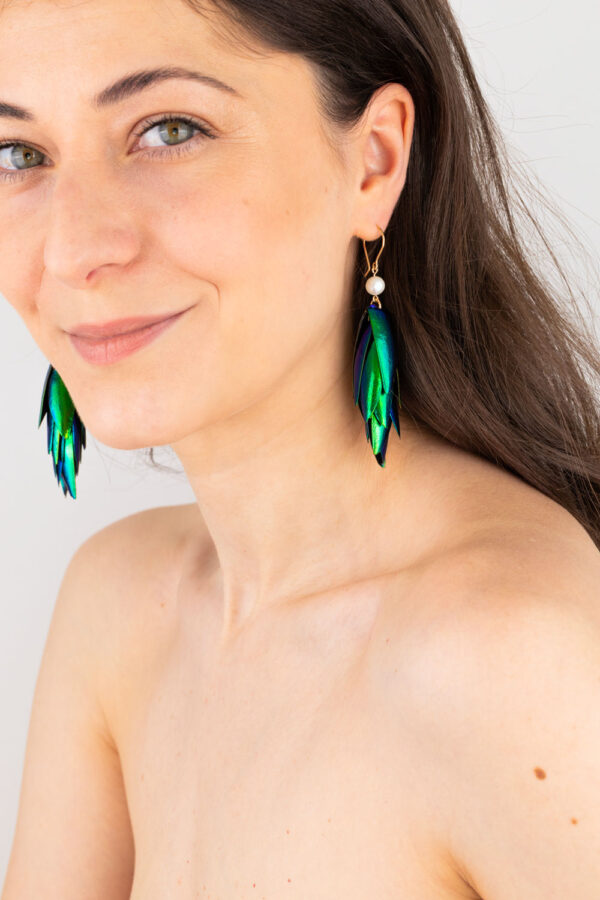 Close-up of white pearl beetle earrings showing colorful reflections